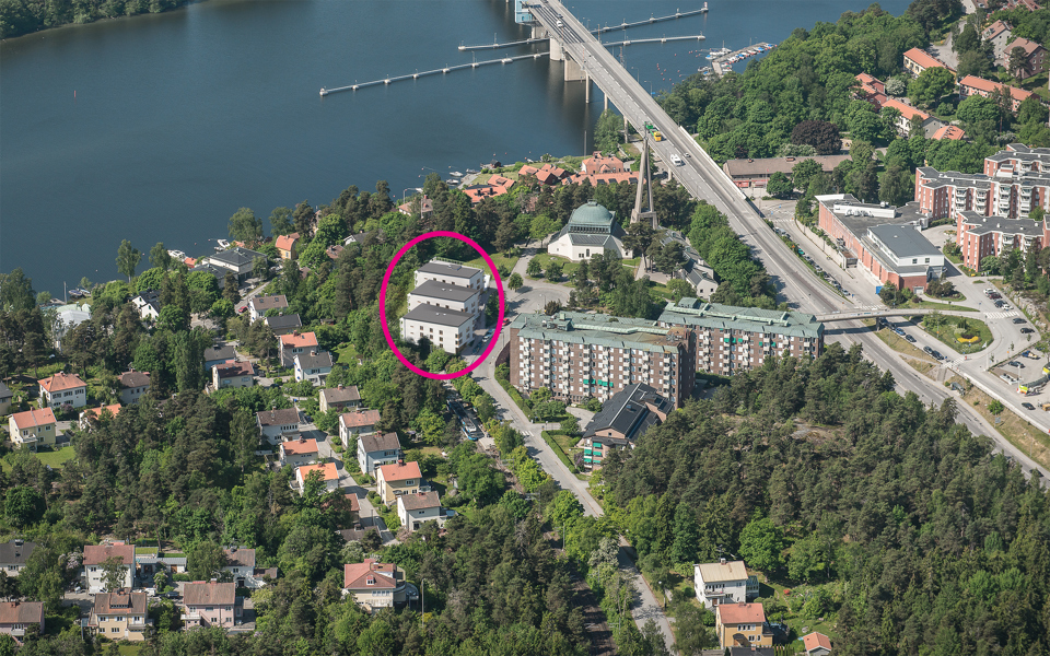 Flygbild över Nockeby med bostadshus, grönområden och Nockebybron. Tre bostadshus markerade i en röd cirkel. Illustration/foto